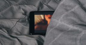 Une tablette est déposée sur un lit, une image de femme apparaît à l'écran. 